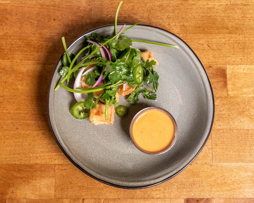 Crispy fried tofu with fresh cilantro, red onion, jalapeño, and a side of orange dipping sauce.