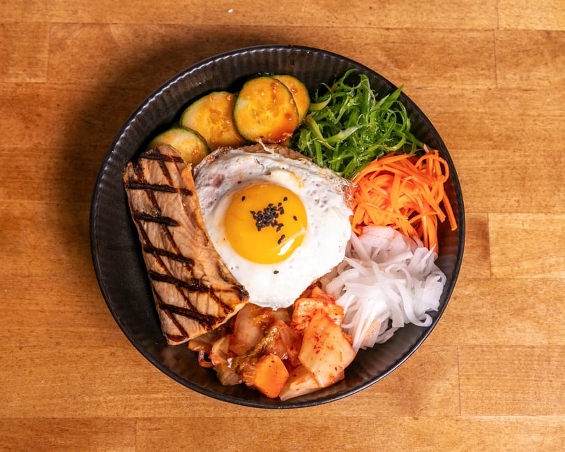 A colorful bibimbap bowl with grilled salmon, fried egg, kimchi, and various vegetables.